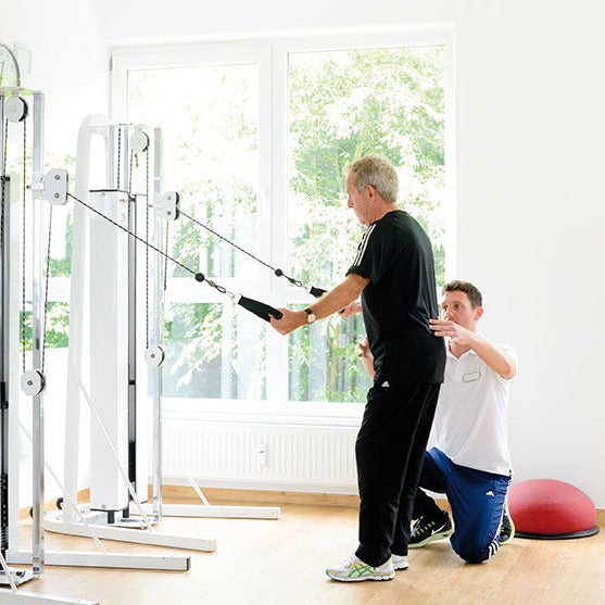 Medizinische Trainingstherapie: Physiotherapeut leitet Patient bei Kabelzugübung an während MTT-Training im ZAR Ulm.